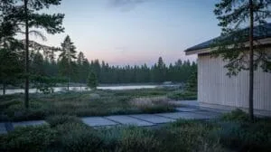 A white cabin with a dark roof sits on the right side of a path made of large, flat grey stones, leading towards a calm body of water surrounded by de