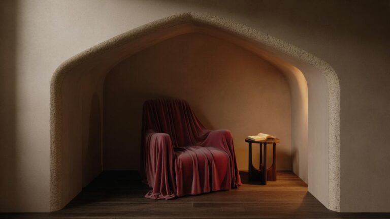 A cozy alcove features an armchair draped in a rich burgundy cloth, accompanied by a small round side table with an open book, all softly lit by warm, ambient lighting.