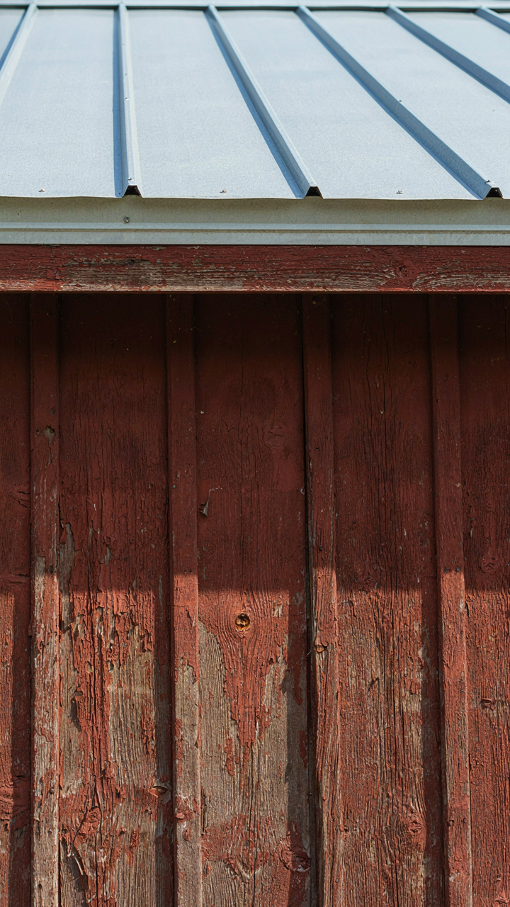 Weathered wood siding with peeling paint contrasts with a clean metal roof.