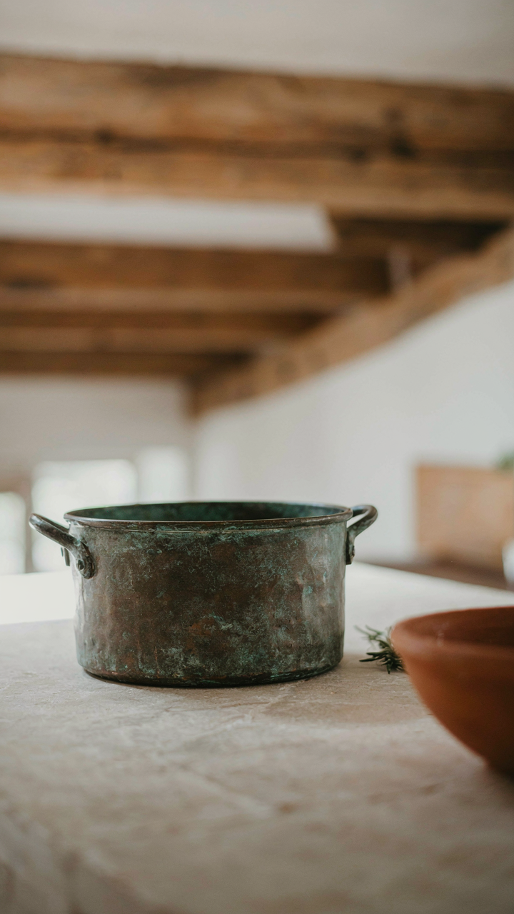 A patinated copper pot sits on a stone counter in a barn house kitchen.