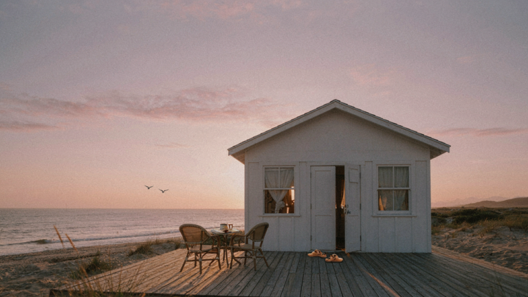 A small beach bungalow with a deck facing the ocean at sunrise.