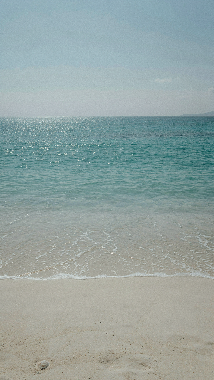 Sunlight intensely reflecting off a bright blue ocean and white sand.