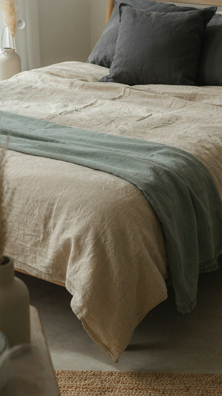 A bed with warm cream, cool sage, and charcoal linen textiles in a bedroom.