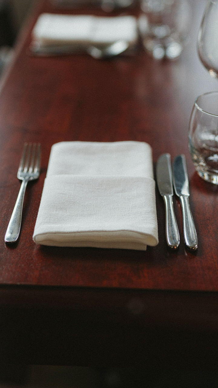 Close-up of a dark wood table with shining silver and a white napkin.