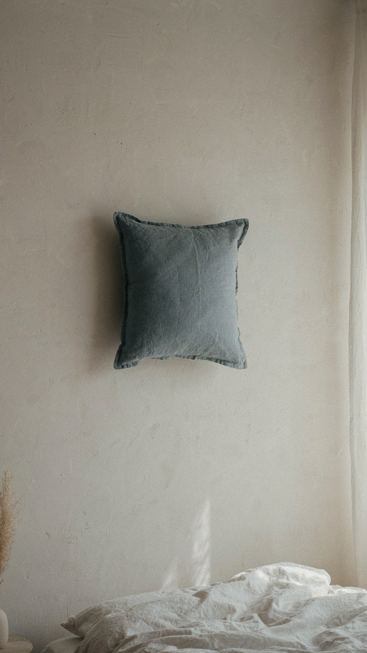 A bedroom wall in soft off-white, with a dusty blue accent pillow on the bed.