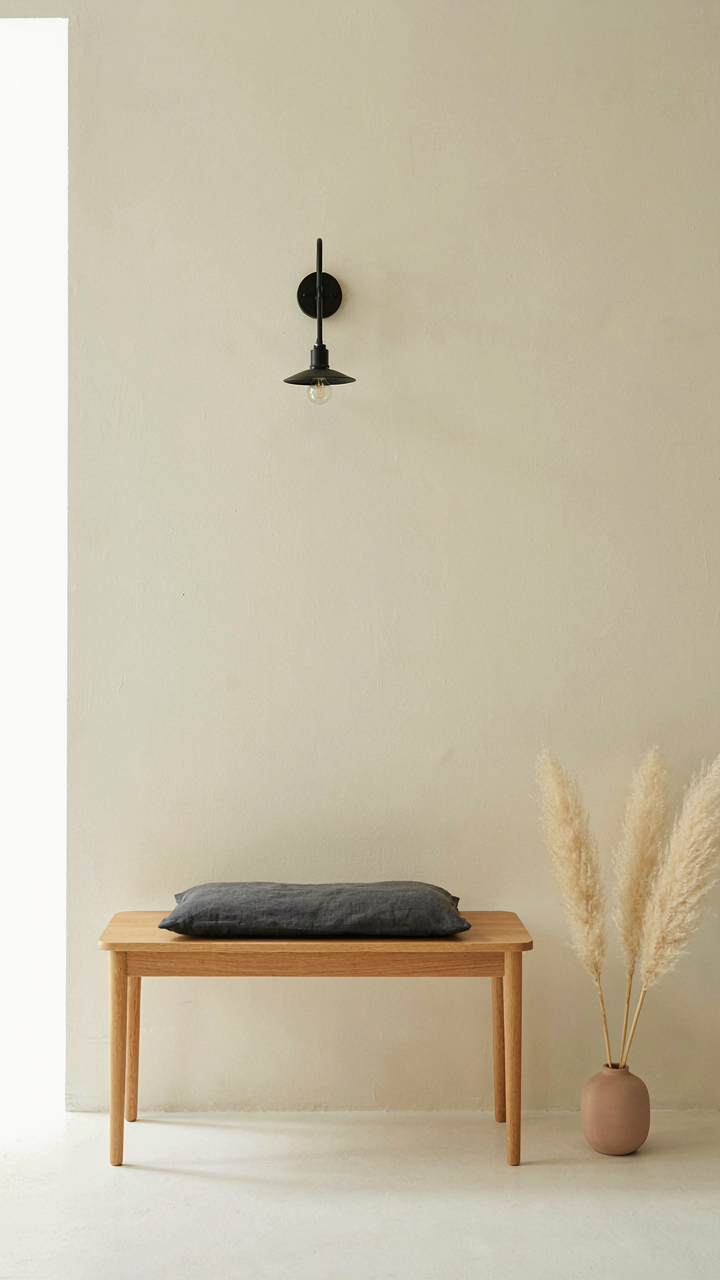 Light wood bench with a dark cushion and a black wall sconce in a scandinavian guest house.