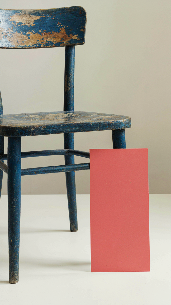 A hand touches an antique painted chair next to a modern paint swatch.