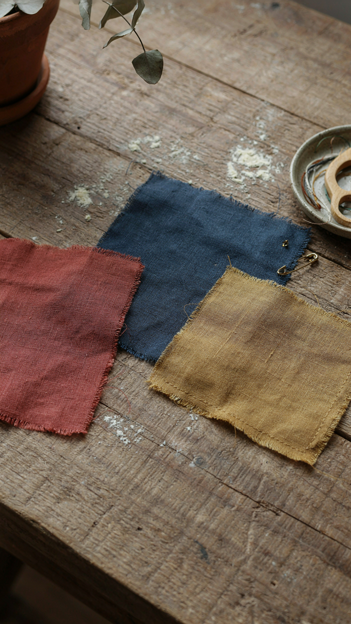 Muted fabric swatches in red, blue, and ochre on a wooden table.