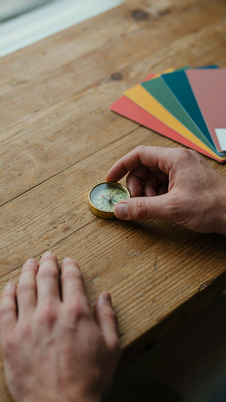 A hand holds a compass pointing to a colorful paint swatch.