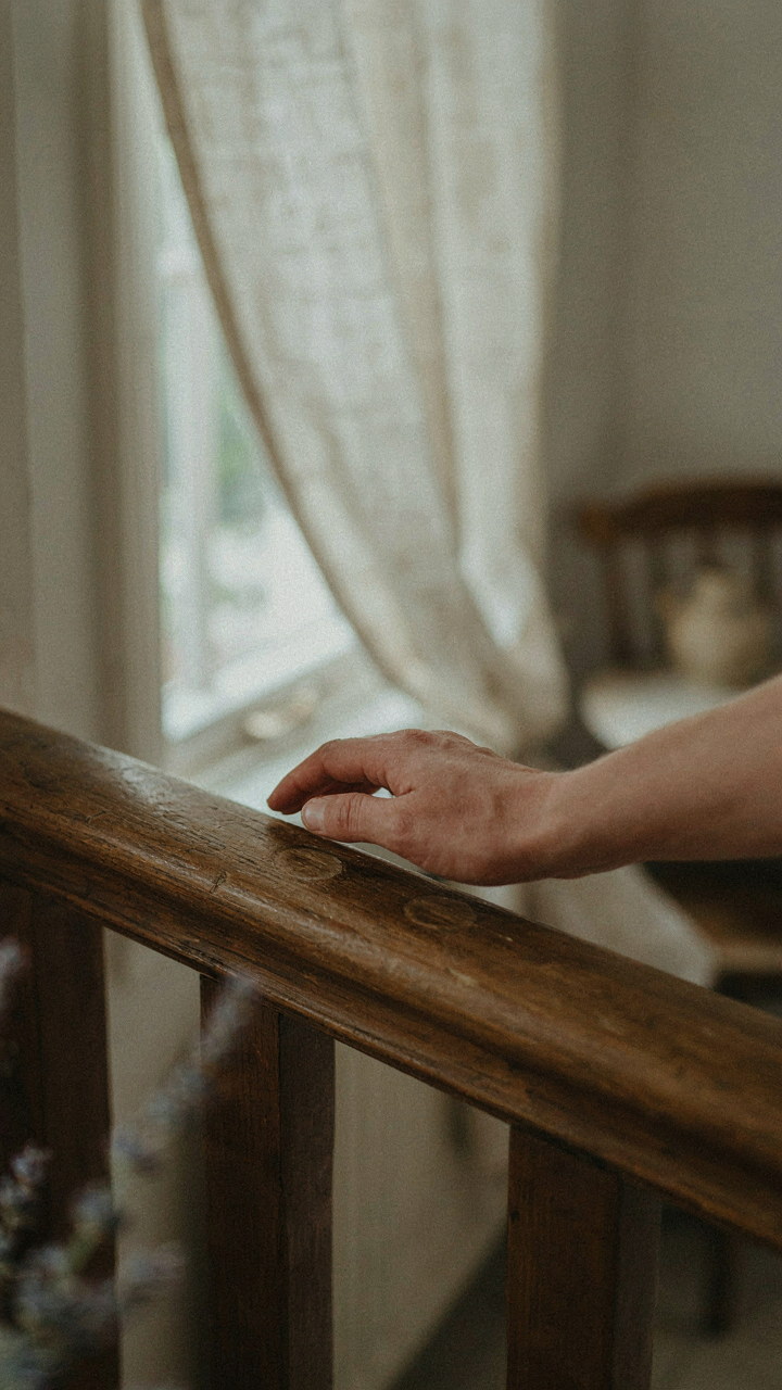 A hand rests on a worn wooden banister in a country home interior.