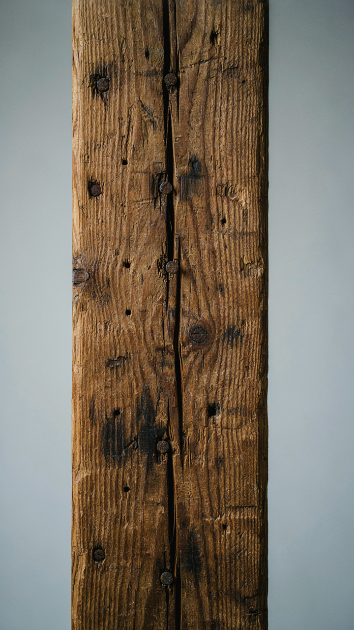 A close-up of a reclaimed wooden beam shows old nail holes and natural patina.
