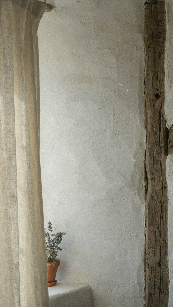 Natural materials like linen, wood, and plaster interact with light in a white cottage.