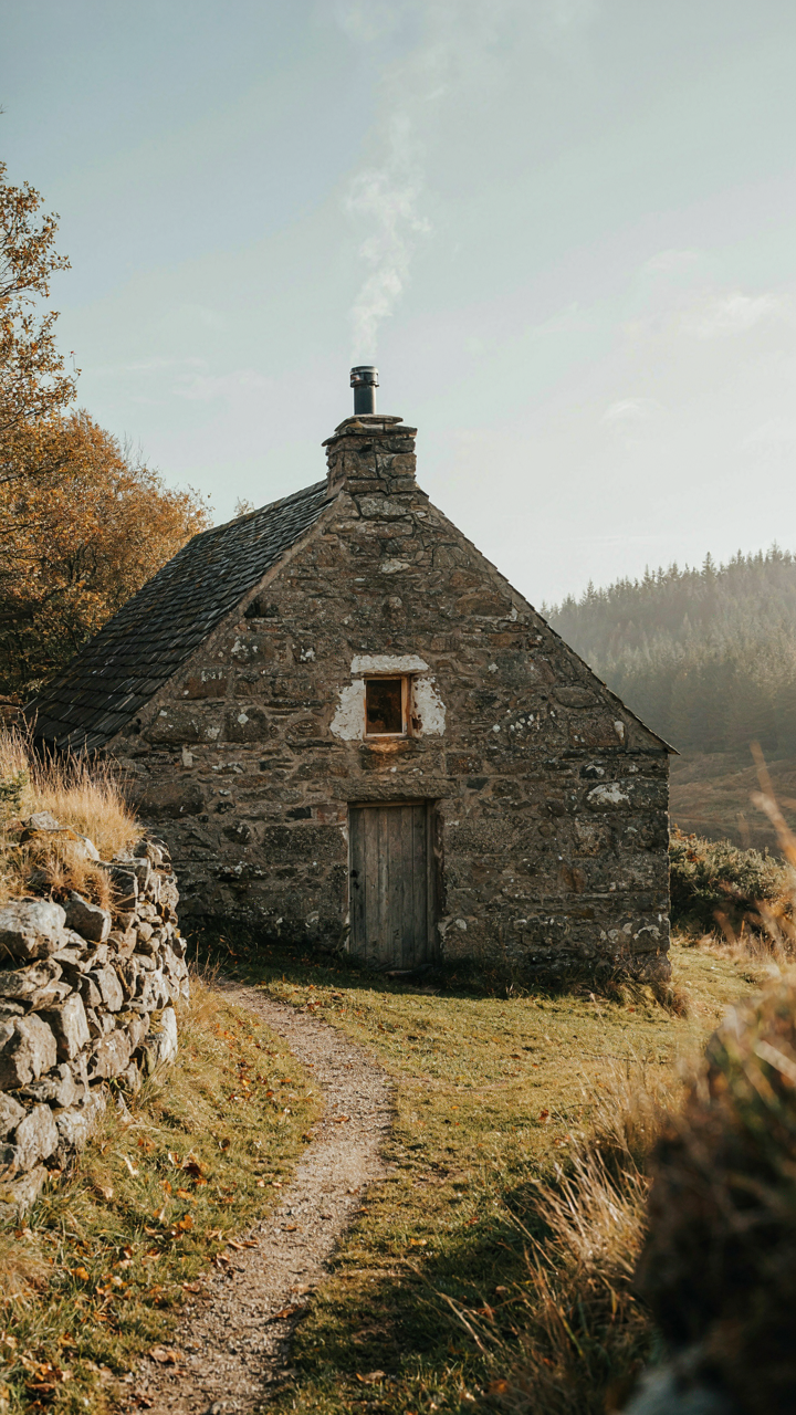 A weathered stone cottage has a steeply pitched roof designed to shed snow.