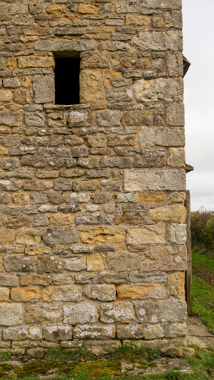 A thick stone wall with a small window in an old British farm house.