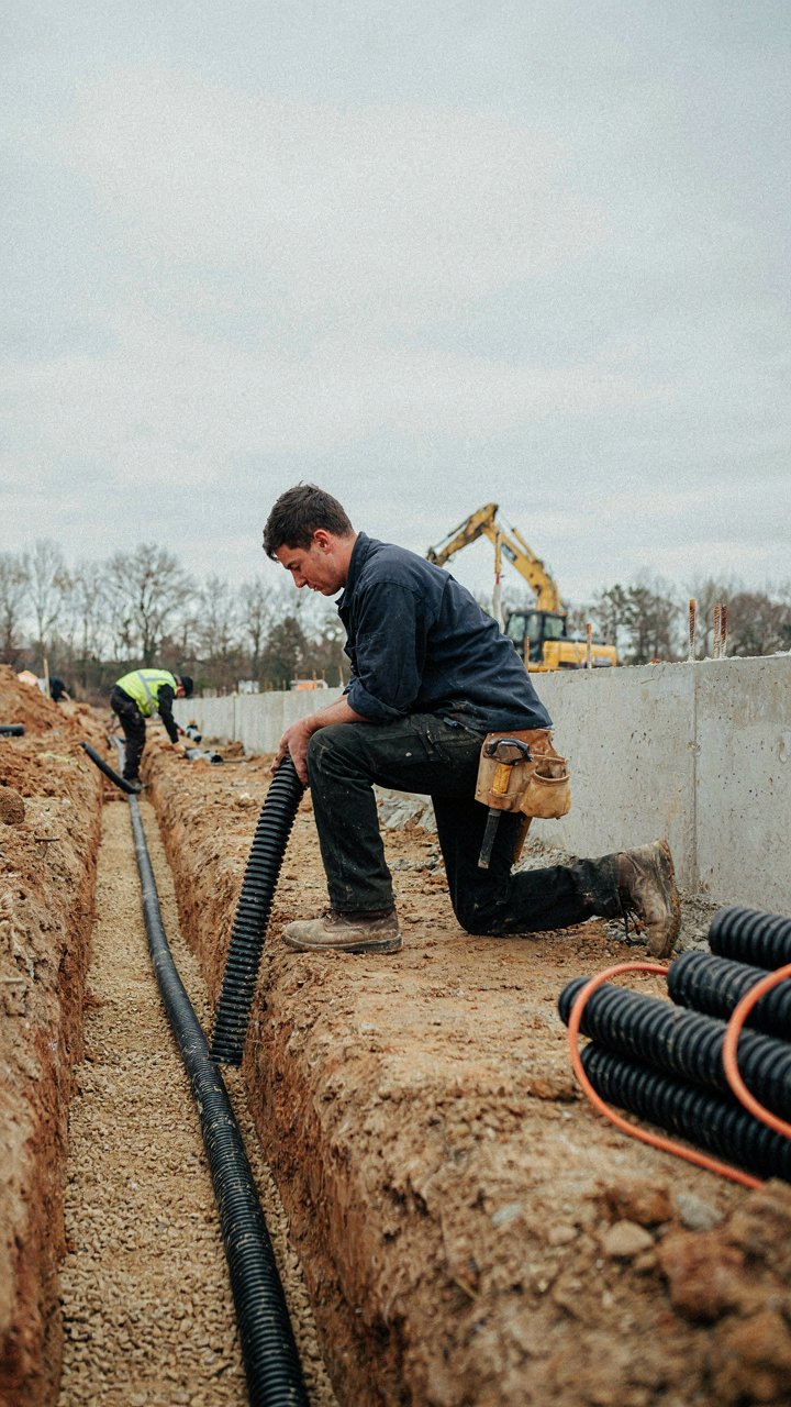 A worker installing drain tile around a cottage foundation.