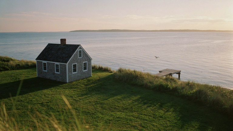 A classic white cape cod cottage with a steep roof, small windows, and cedar shingles by the sea.