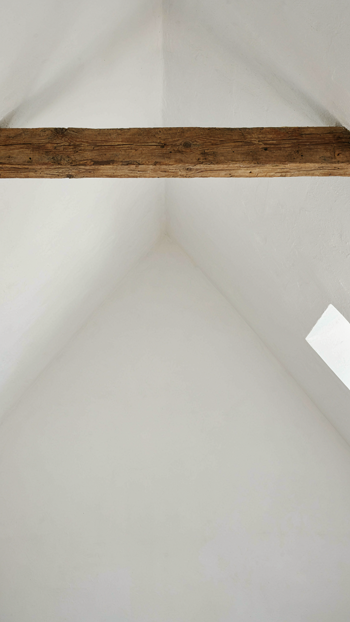 A single, aged reclaimed timber beam spans a white vaulted ceiling.