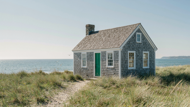A charming coastal cottage with gray shingles and a green door by the ocean.