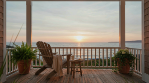 A beautiful coastal cottage porch with a view of the ocean at sunset, comfortable seating.
