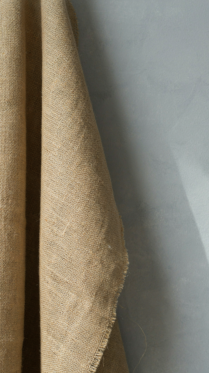 Rough burlap fabric rests against a soft gray painted wall.
