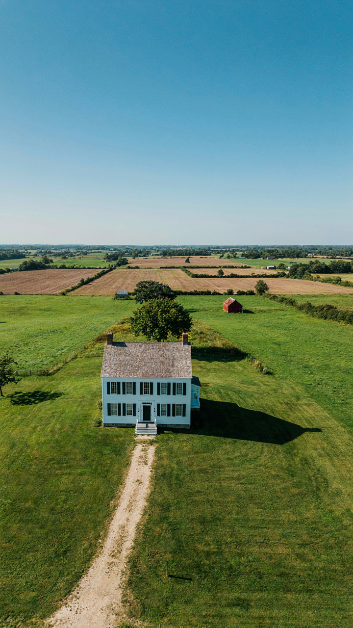 Aerial view of a colonial farmhouse on a rise, facing south.