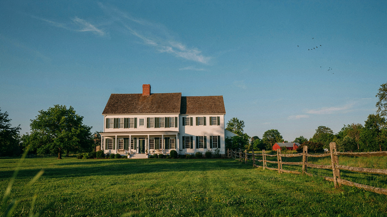 Classic white colonial farmhouse in a field with a prominent central chimney.