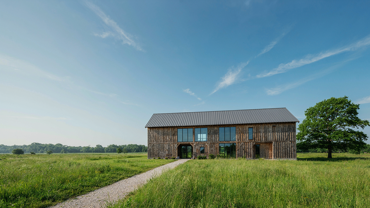 A beautiful converted barn home combines old timber with new glass in a green field.