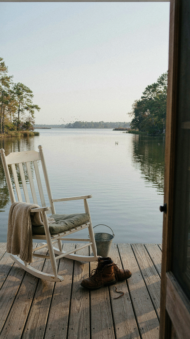 Rocking chair on a deep porch overlooks a calm lake and trees.