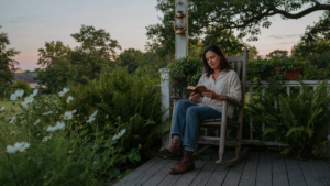 A person relaxes in a rocking chair on a peaceful country porch at sunset.