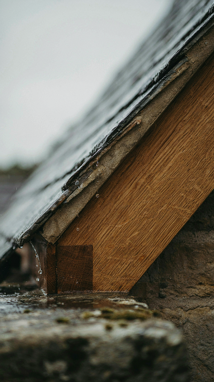 A close-up of a robust, exposed wooden rafter tail shedding rainwater.