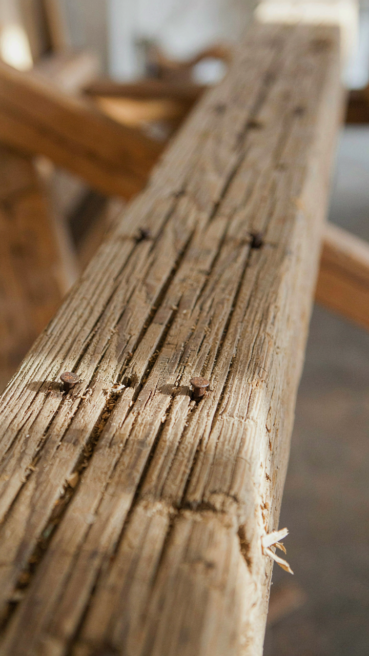 A close-up of a reclaimed wood beam shows its weathered texture and nail holes.