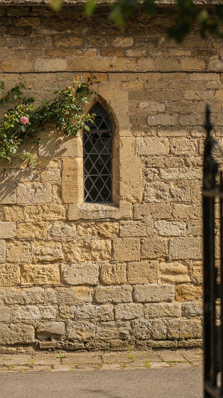 An old English cottage wall made of uneven, honey-colored stone.