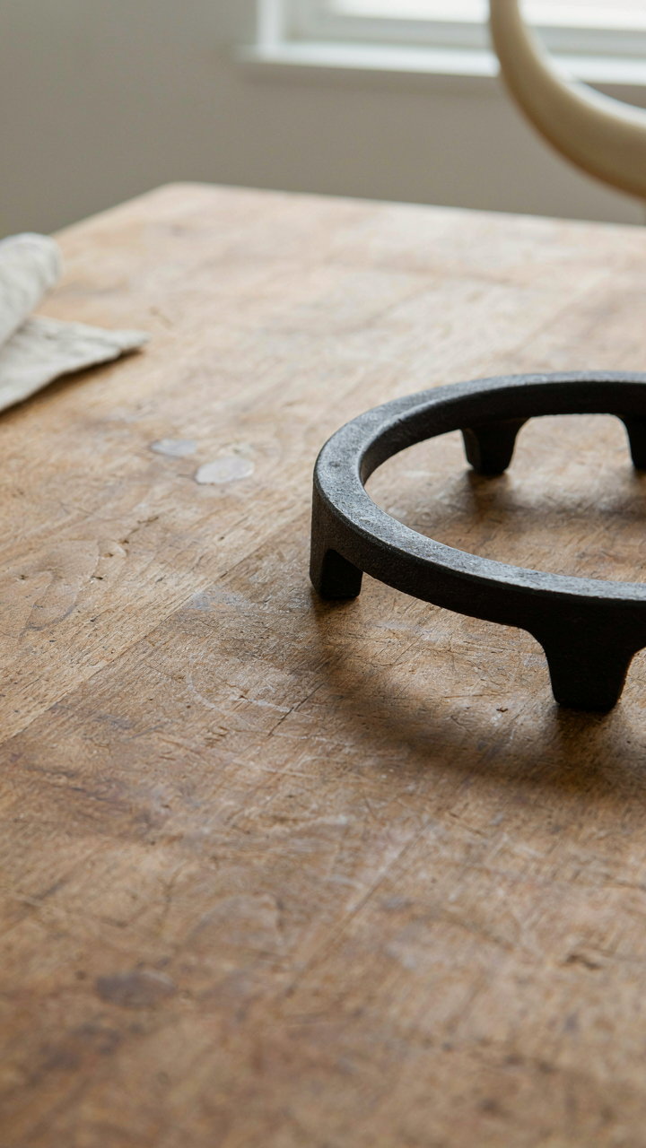 A close-up of a durable wooden dining table with a metal trivet.