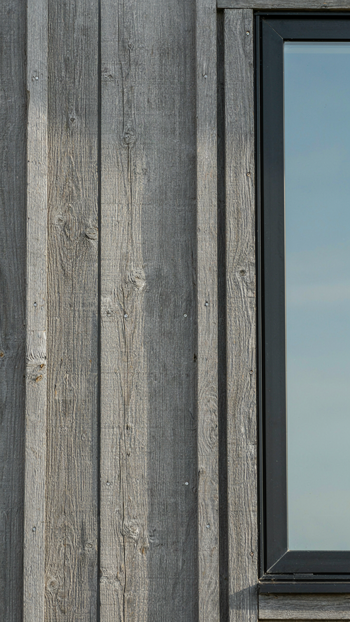 Weathered barn siding meets a large modern black-framed window with a clean line.