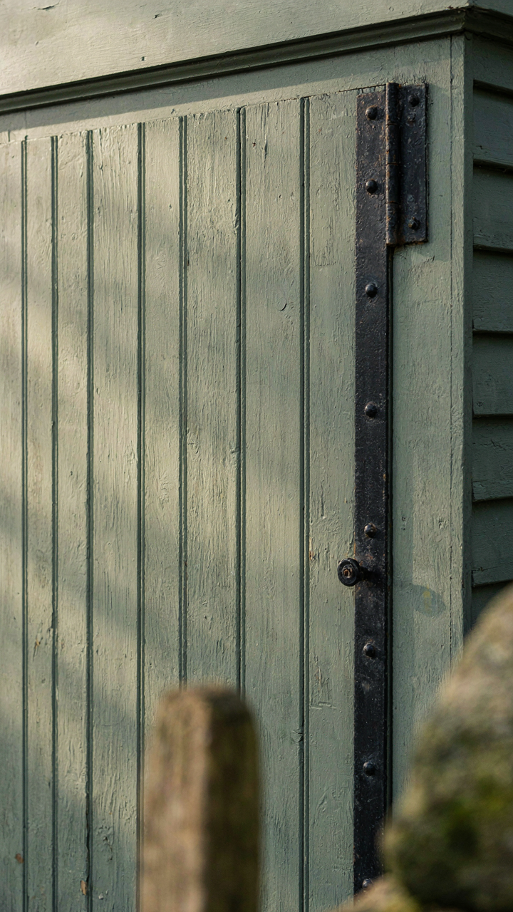 A shiplapped shed door with heavy black cast iron strap hinges and substantial trim.