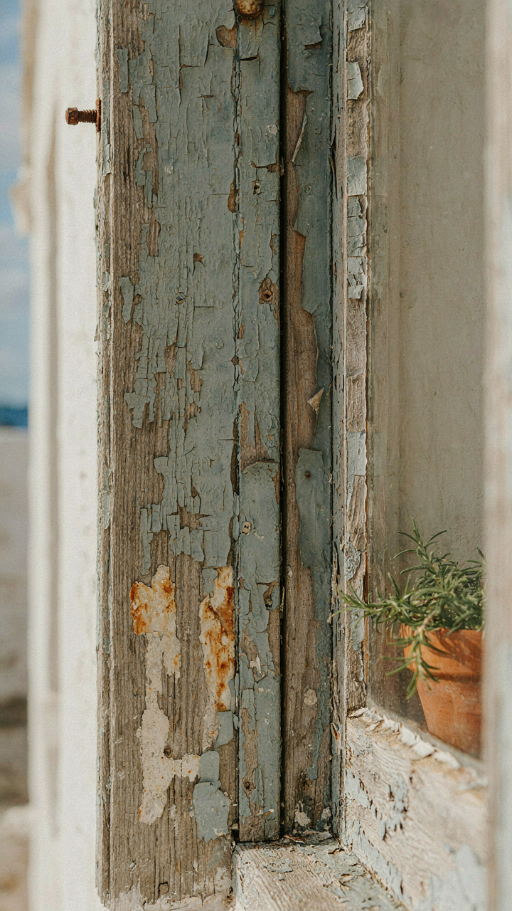 A weathered wooden window frame shows visible salt stains and peeling paint.