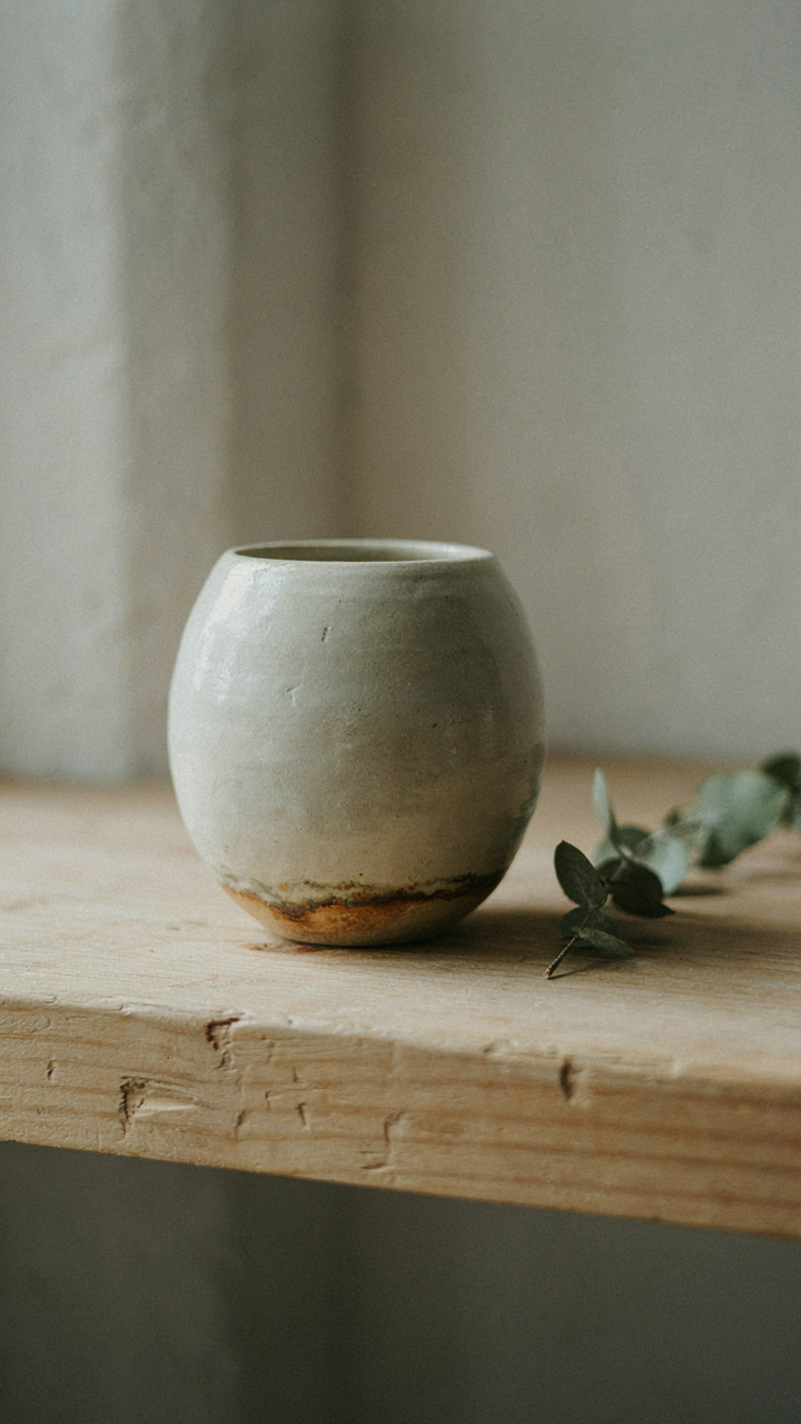 A handcrafted ceramic pot with flaws on a rustic wooden shelf.