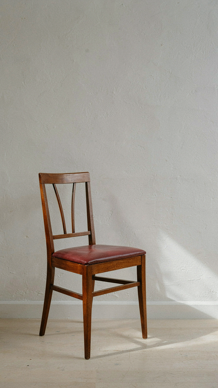 An elegant mahogany dining chair with simple lines sits against a plain wall.