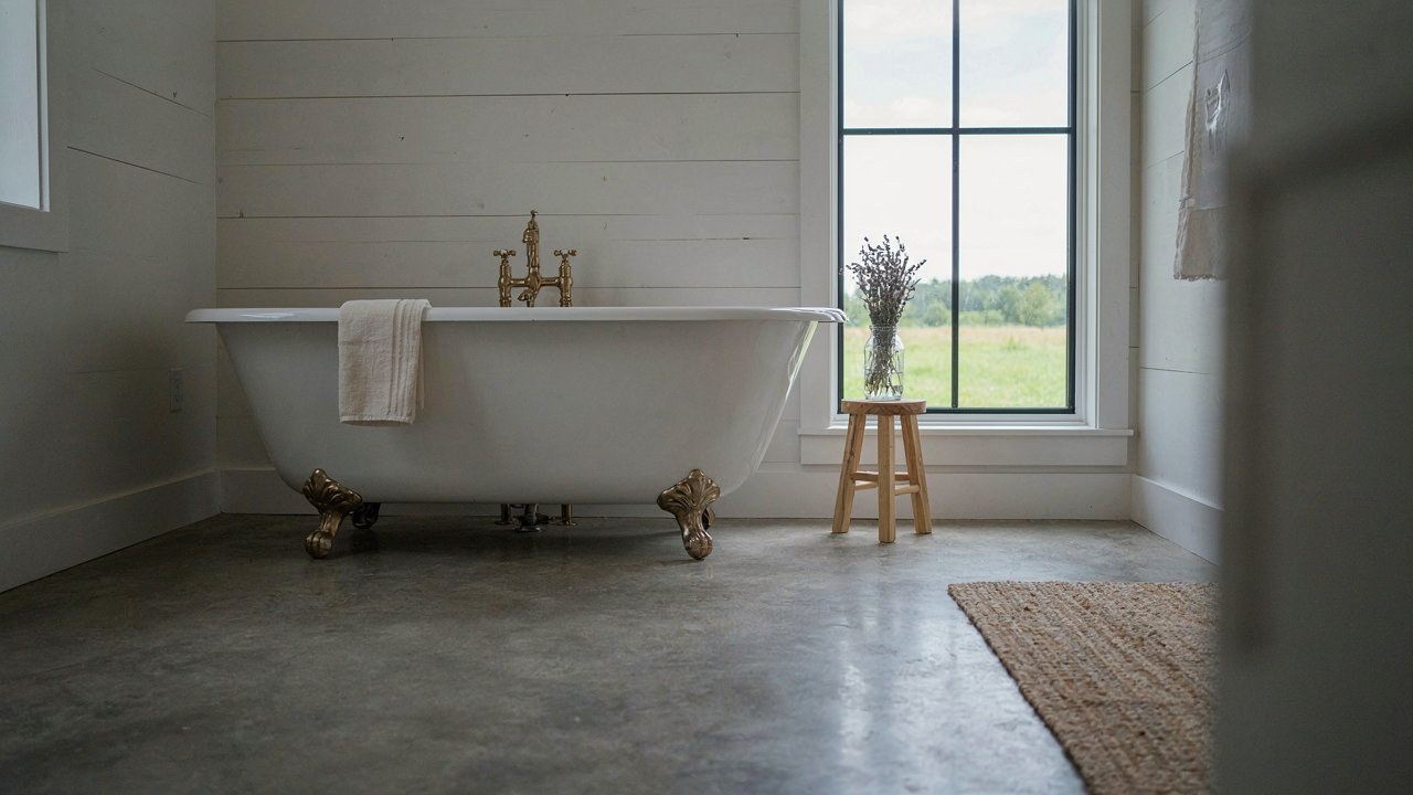 A serene farmhouse bathroom featuring a concrete floor and a classic white clawfoot tub.