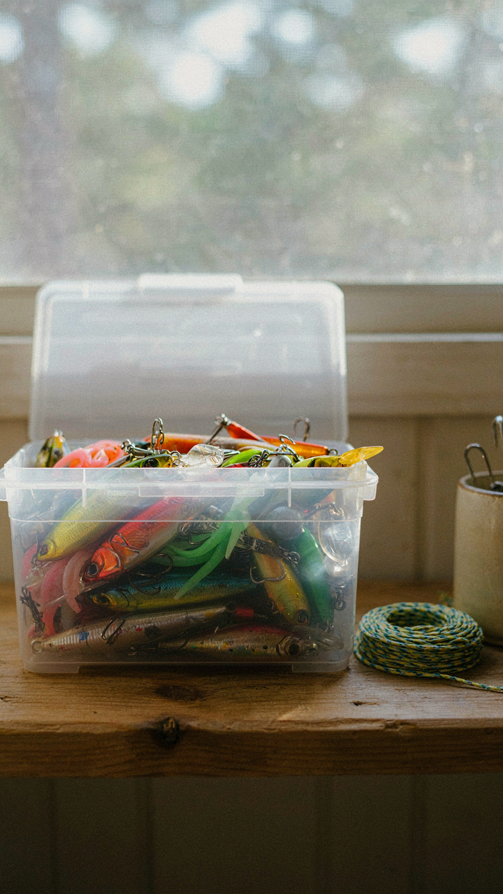 Clear plastic bins with labeled fishing lures on a shelf in a fishing cabin.