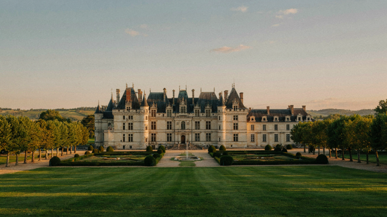 A grand French chateau with turrets stands under a golden sky, surrounded by manicured gardens.