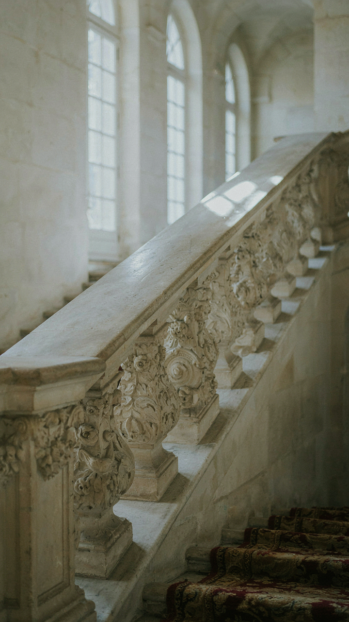 An intricately carved limestone balustrade on a chateau staircase shows detailed floral patterns.