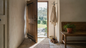 A rustic french country entryway with a wooden door, stone floor, and a simple iron coat rack.