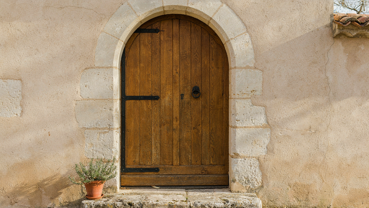 A rustic french country front door made of oak, with iron hinges and a stone archway.