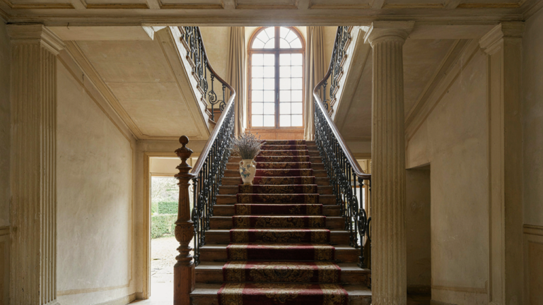 A sweeping French country staircase with elegant iron and warm wood in a sunlit hall.