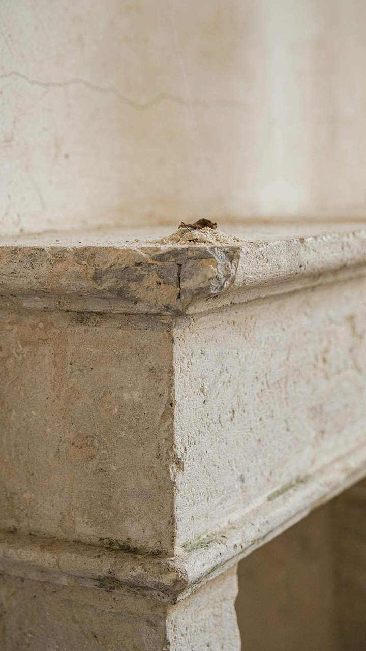 A close-up of a weathered limestone mantelpiece with a chipped edge.