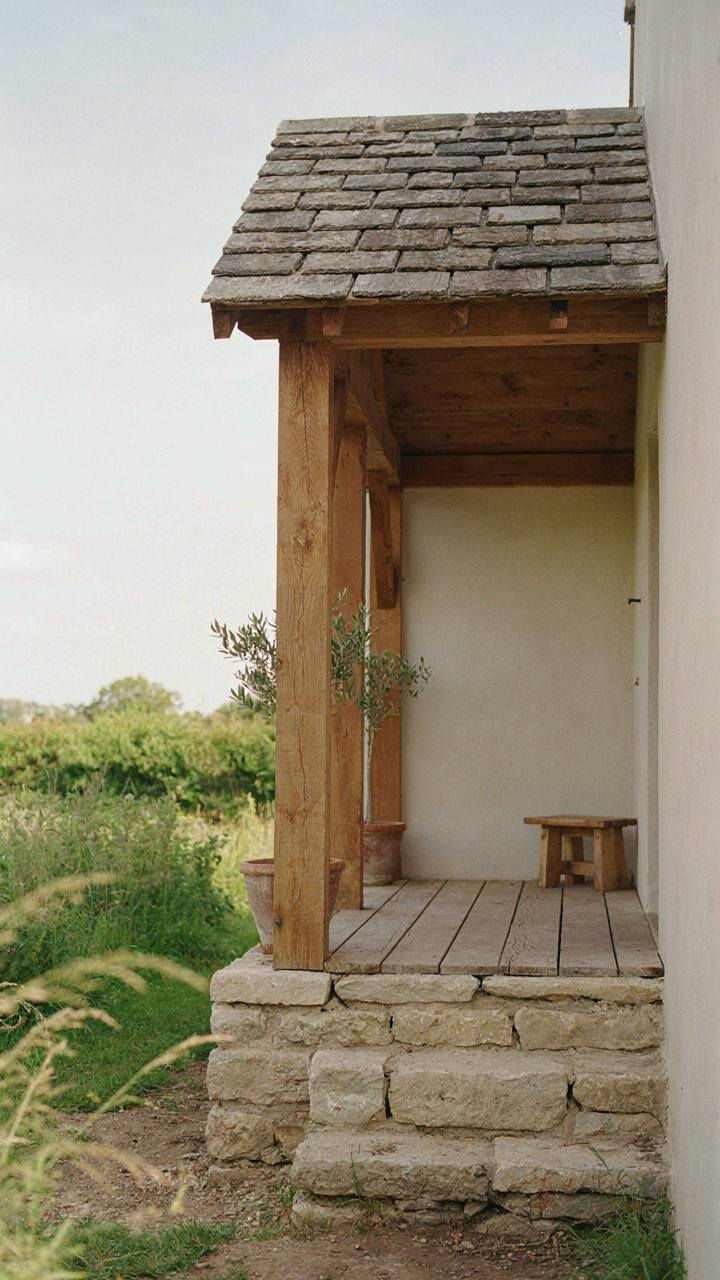 A minimalist cottage porch shows raw wooden beams and stone steps.