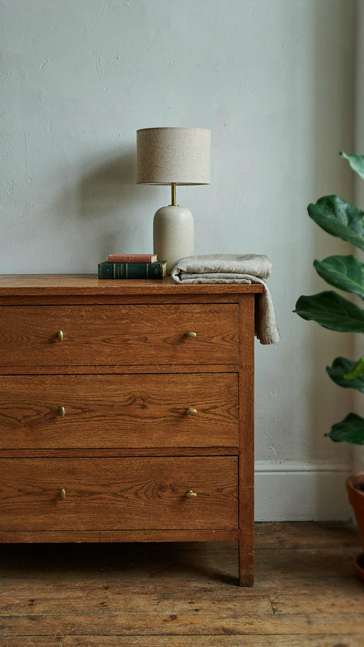 A solid oak dresser with rich grain and a simple ceramic lamp on its surface.