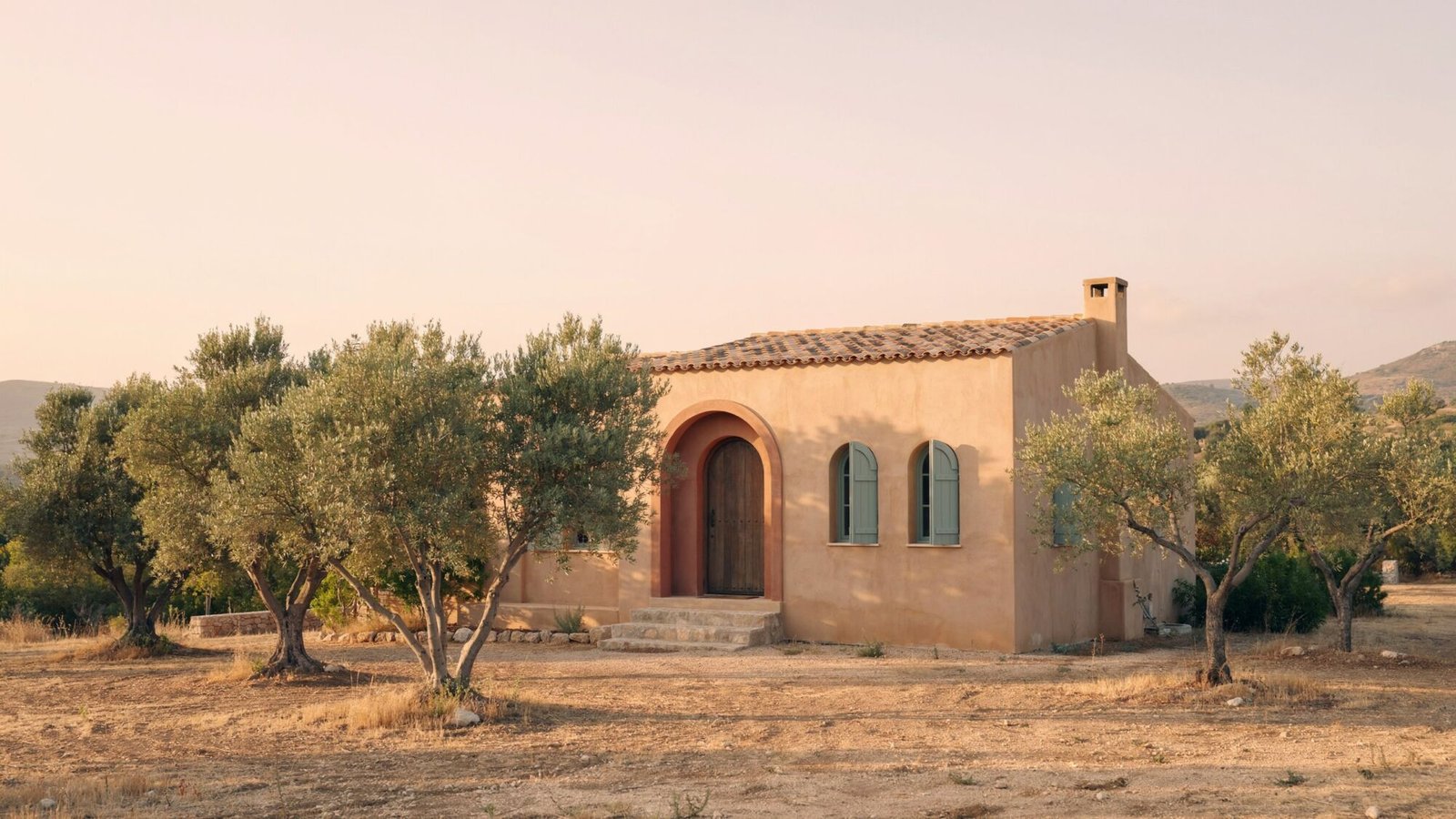 Sand stucco home with an arched doorway among olive trees at golden hour