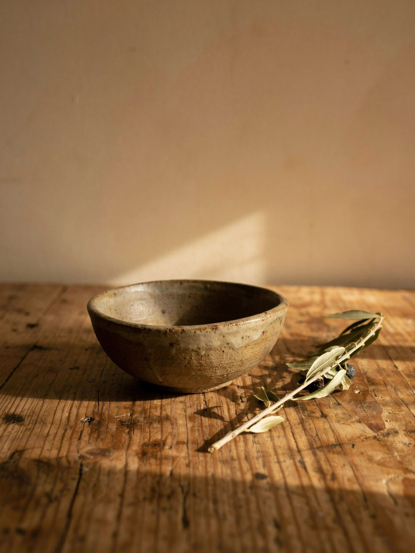 Handmade ceramic bowl and dried olive branch on a reclaimed oak table